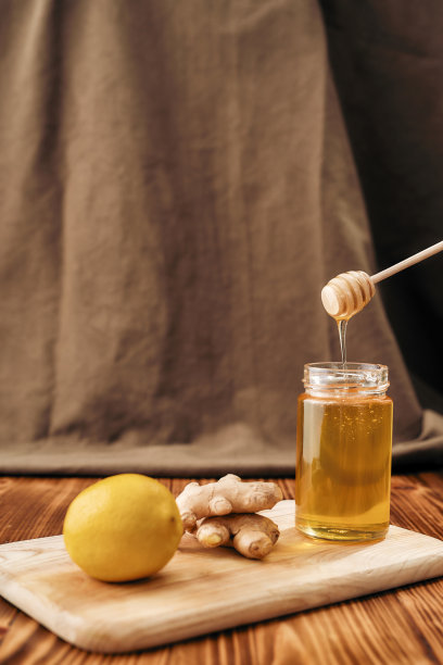 将新鲜的生姜、柠檬、蜂蜜放在木板上的罐子里，在准备感伤饮料时手拿蜂蜜勺图片下载