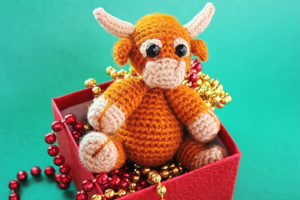公牛是2021年新年的象征。一个编织的玩具公牛在一个红色的盒子里，绿色的背景上有圣诞珠子。图片下载