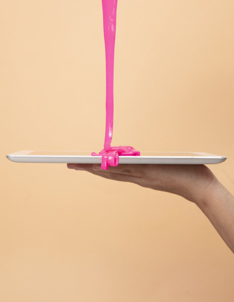 女人的手使用数字平板电脑与霓虹粉色黏液玩具在橙色波普艺术背景。图片下载