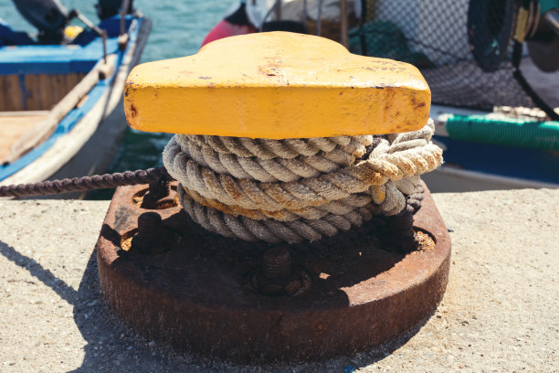 锈迹斑斑的黄色系柱，用结实的缆绳系泊港口内的渔船图片下载