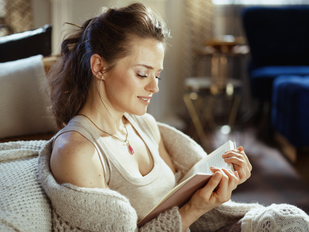 微笑的女性在阳光明媚的秋日在现代的房子里看书图片下载