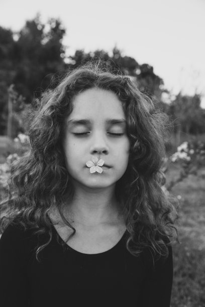 一个漂亮的小女孩的近距离肖像闭着眼睛捧着一朵花在嘴里。黑白图像。图片下载