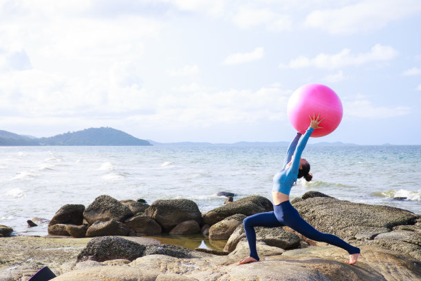 年轻的亚洲女人练习瑜伽与健身球在海滩上。放松,健康的概念。图片下载