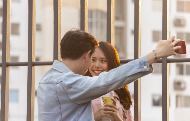 在情人节甜蜜晚餐上，可爱的亚洲男友用智能手机与女友自拍图片下载