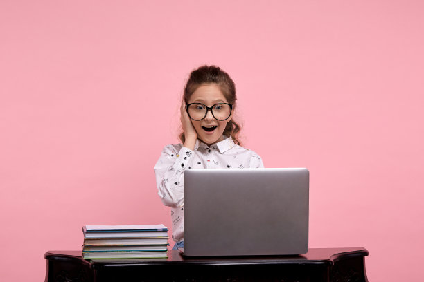 惊讶的女孩坐在桌子旁边，拿着笔记本电脑，一只手拿着眼镜图片下载