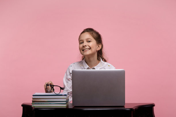 一个小女孩坐在笔记本电脑前，看着镜头学习。图片下载