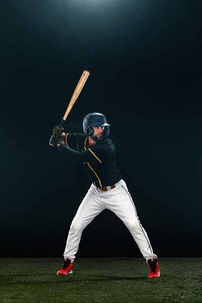 在黑暗背景上使用球棒的棒球运动员。参加球赛的肖像。图片下载
