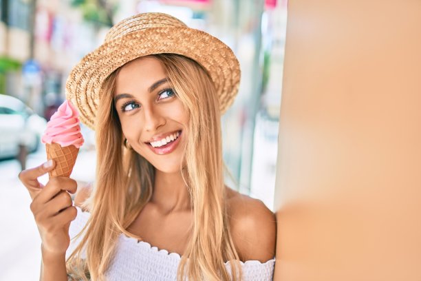 年轻的金发女游客愉快地靠在墙上吃着冰淇淋。素材图片