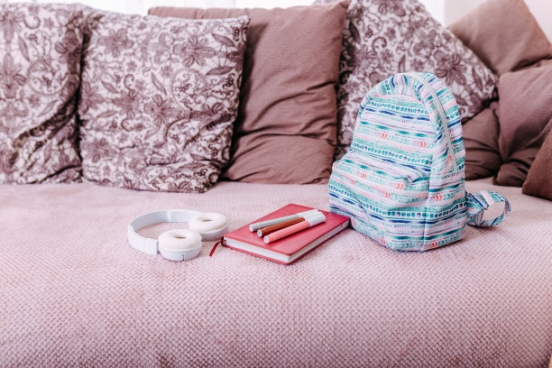 放学后把学习用品平躺在沙发上。蓝色背包，白色耳机，笔记本和笔。图片下载