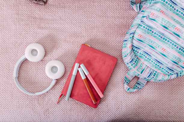 放学后把学习用品平躺在沙发上。蓝色背包，白色耳机，笔记本和笔。图片下载