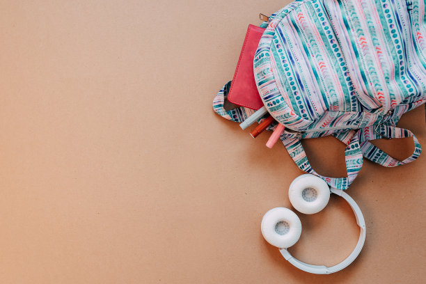 学校用品平铺在牛皮纸背景上。蓝色背包，白色耳机，笔记本和有拷贝空间的笔。图片下载