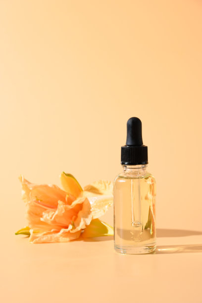 化妆油或香精玻璃瓶与新鲜的百合花在米色背景。垂直的。关闭了。图片下载