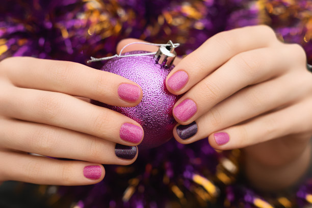 圣诞节钉的设计。女性的手用粉红色和棕色美甲。女人拿着圣诞玩具球。图片下载