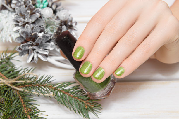 女性的手与圣诞钉子设计。绿色指甲油美甲。女人手里拿着绿色的清漆。图片下载