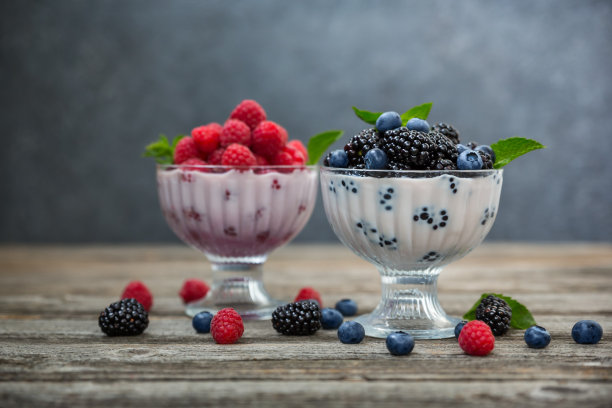 甜点奶油，覆盆子，蓝莓和黑莓，在玻璃花瓶上的木制背景。图片下载