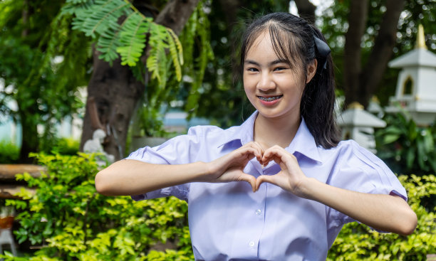 画像泰国初中学生制服美丽的女孩戴着牙套美丽的微笑使手手势在心形爱的标志概念图片下载