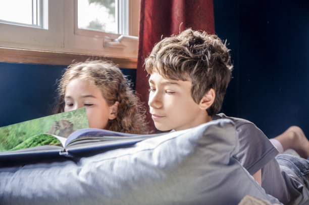 年轻的女孩和男孩在她的床上看书图片下载