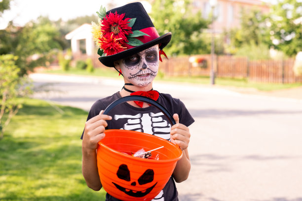 男孩画着脸，穿着黑色万圣节t恤，戴着优雅的帽子，拿着糖果图片下载