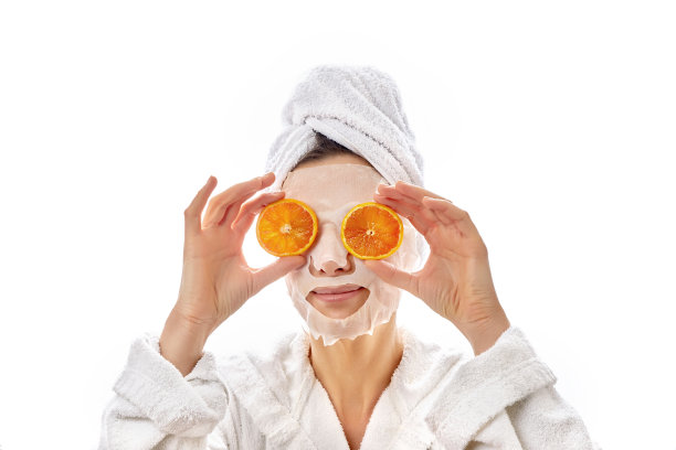 漂亮的女人拿着一条白毛巾，眼睛旁边放着几片亮橙色的肉。孤立在白色背景上。图片下载