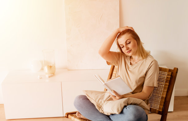 年轻女子在家里坐在现代椅子在窗前放松在她的客厅看书素材图片