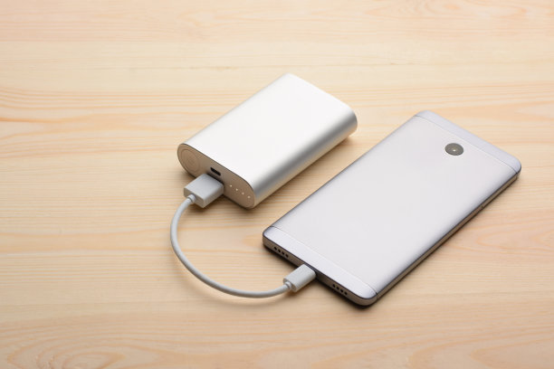 现代银色智能手机放在轻木桌上，后面板向上，同时用电源充电图片下载