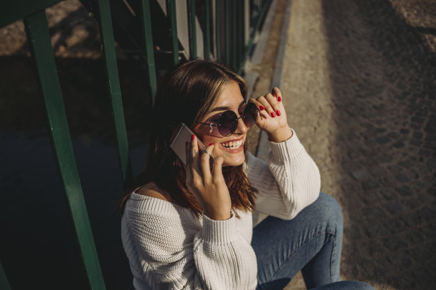 一个时髦的年轻女孩正坐在城市的一座桥上用手机休息图片下载