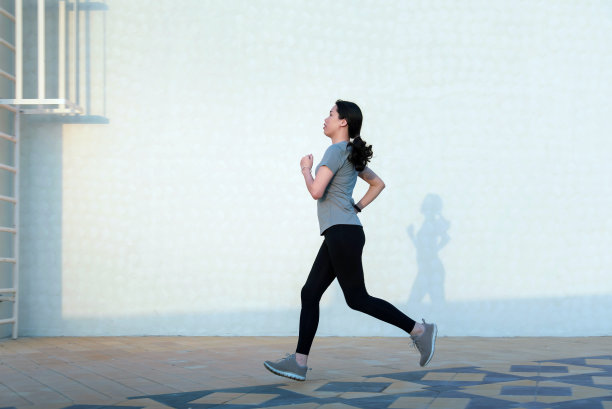 在户外对着白色墙壁慢跑的女人，留有文案空间素材图片