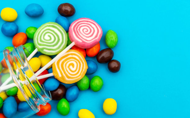 糖果从玻璃罐中散落在蓝色背景上。关闭了。空间的文本。图片下载