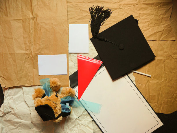 毕业布置平铺地板，地板上放着泰迪熊、方学位帽、红旗和证书图片下载