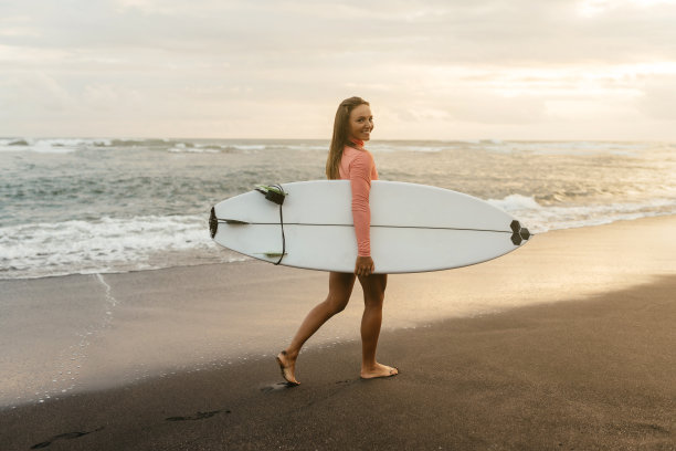 年轻迷人的冲浪女子与白板在日落的海洋上。印度尼西亚巴厘岛。图片下载