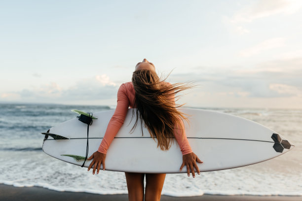 年轻迷人的冲浪女子与白板在日落的海洋上。印度尼西亚巴厘岛。图片下载