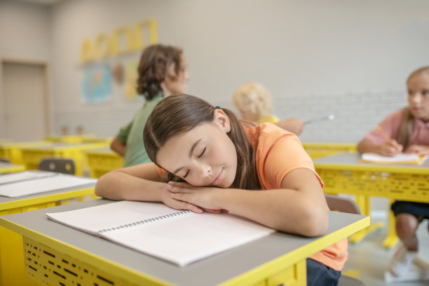 穿着橙色t恤的黑发女孩睡在桌子上图片下载