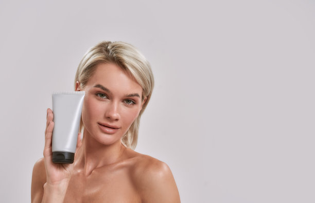 年轻女人的肖像与完美的新鲜的皮肤看着相机，拿着和广告化妆品护肤，身体护理产品，而摆出孤立的灰色背景图片下载