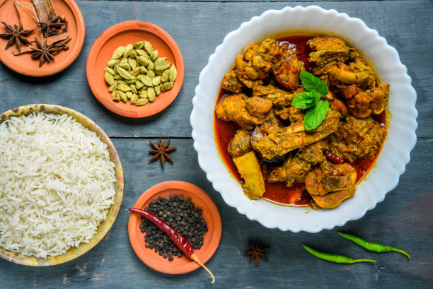 咖喱鸡或香料，辣红鸡腿片配香菜叶，安排在一个白色陶瓷碗与木制背景图片下载