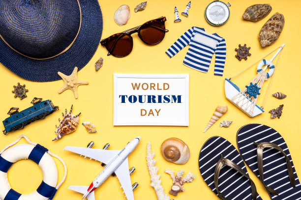 世界旅游日快乐。色彩柔和的旅游服饰、帽子、人字拖、太阳镜和装饰物。平躺，俯视图。世界旅游日白色文字相框图片下载
