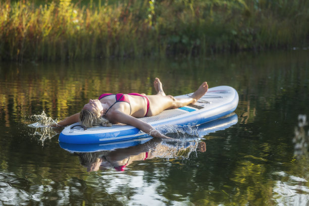 快乐的女人享受在湖上冲浪板日光浴图片下载