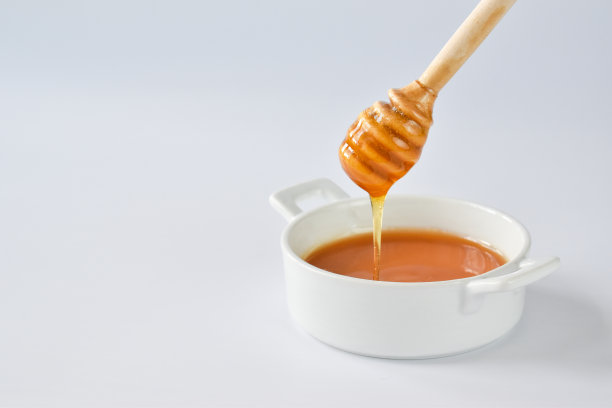 蜂蜜顺着木勺流进白底的碗里。极简主义。图片下载