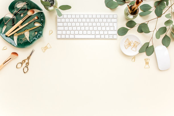 平躺在家办公的书桌。女性工作空间用电脑、板片怪兽、金色配件、桉树叶、米黄色背景。俯视图图片下载