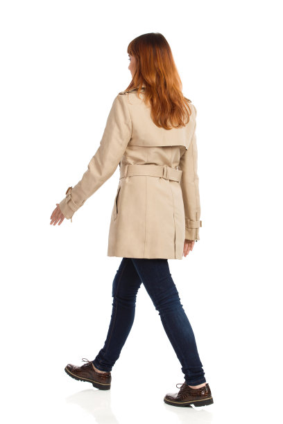 走路的年轻女子米色外套，牛仔裤和棕色鞋子。后侧的观点。图片下载