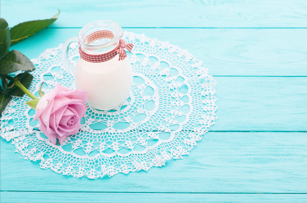 午餐时间，牛奶罐，粉红玫瑰和格子丝带在蓝色木制背景。花边台布。有选择性的重点。情人节和母亲节图片下载