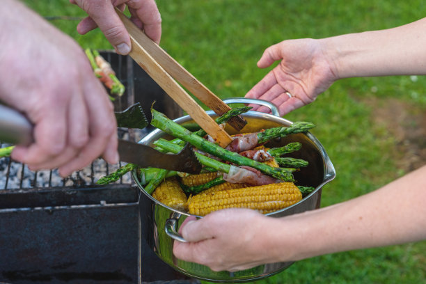 美味烧烤。烤蔬菜——玉米、芦笋配培根和意大利熏火腿。男人和女人一起做饭。在女人的手锅烧烤。共同的生活方式。图片下载