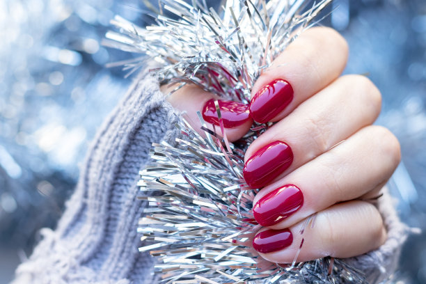 女性手在灰色针织毛衣与美丽光滑的指甲-酒红色，深红色，樱桃色的指甲背景银色圣诞金丝花环。有选择性的重点。特写视图图片下载