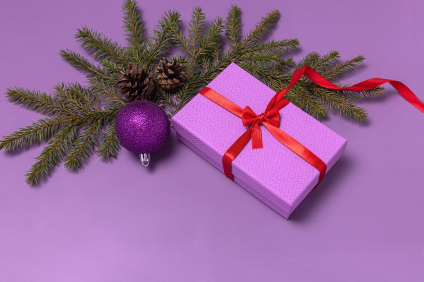 粉红色的礼盒，冷杉树枝和锥形，紫色的圣诞球在紫色的背景图片下载