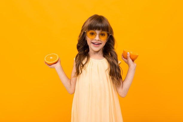 戴眼镜的快乐女孩拿着黄色背景上的橙子图片下载