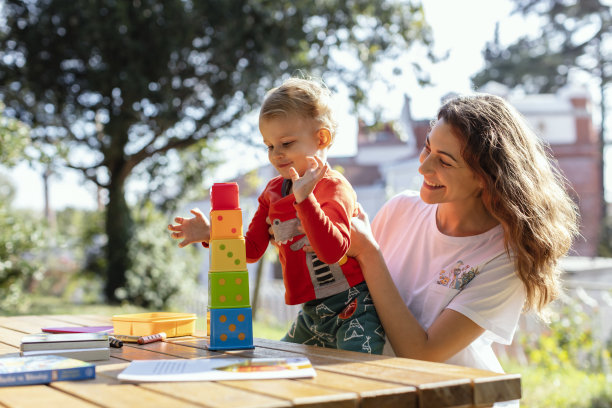 阳光明媚的一天，年轻的女人和儿子在花园里玩益智方块玩具图片下载