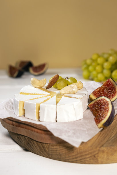 卡芒贝尔奶酪放在木板上，绿葡萄枝，无花果片和坚果。图片下载