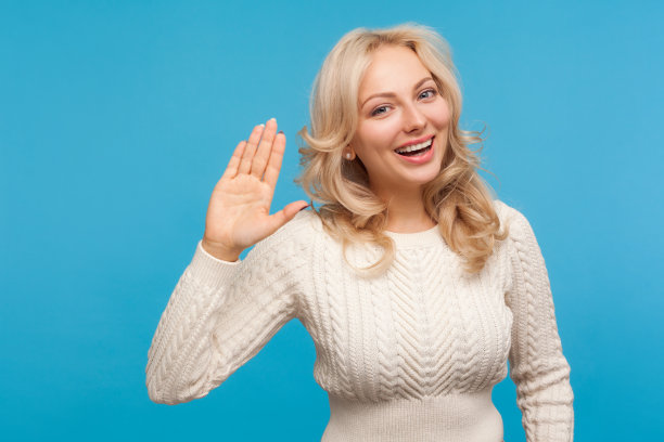 友善快乐的金发女人举起手，露出露齿的笑容，乐观地打招呼图片下载