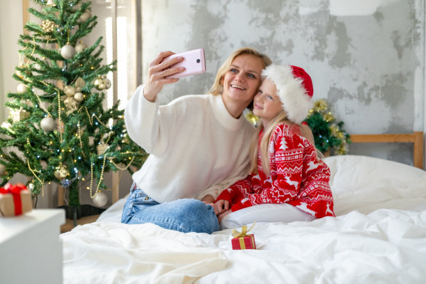 圣诞在线家庭祝贺。微笑的欧洲金发母亲和女儿在圣诞节服装自拍照片图片下载