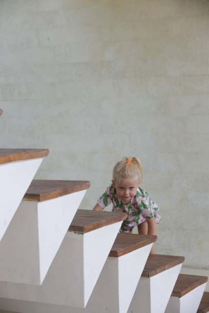 可爱的金发小女孩爬上家里的木楼梯。图片下载