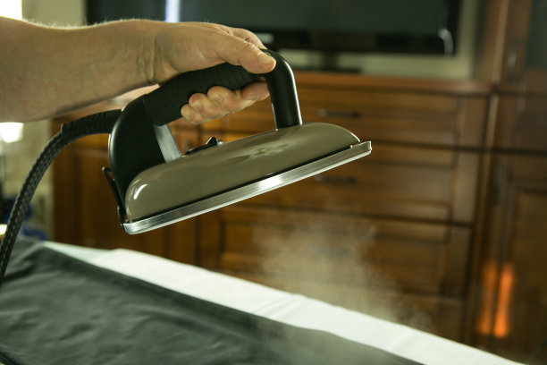 家庭作业。特写镜头，妇女在熨衣板上用熨斗熨烫衣服。蒸汽喷射在照片中清晰可见。图片下载